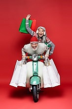 excited middle aged interracial couple in sweaters with shopping bags riding moped on red