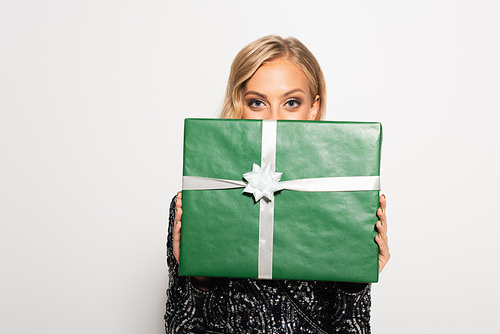 young blonde woman hiding face behind green gift box while  isolated on white