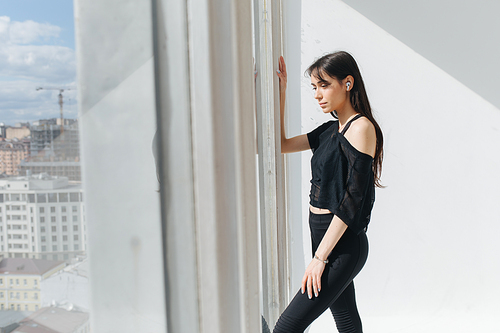 sportive armenian woman in earphone and sportswear dreaming near window