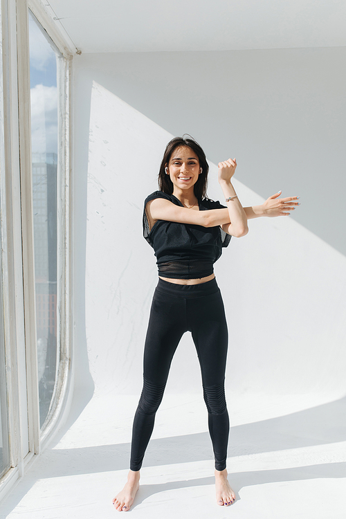 full length view of smiling armenian woman practicing yoga at home