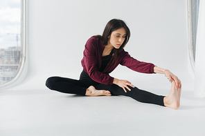 brunette armenian woman practicing seated forward bend pose on white floor