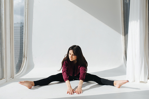 barefoot armenian woman practicing wide-legged forward bend pose on floor near window