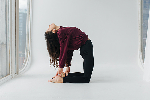 side view of pretty armenian woman practicing camel yoga pose on white floor