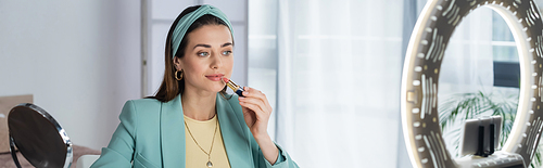 stylish woman applying lipstick near phone holder with ring lamp, banner