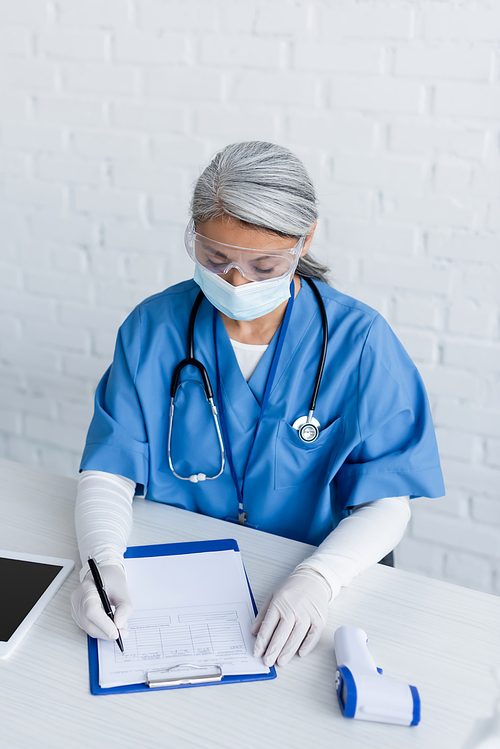 asian immunologist in medical mask, goggles and latex gloves writing on medical card, vaccination concept