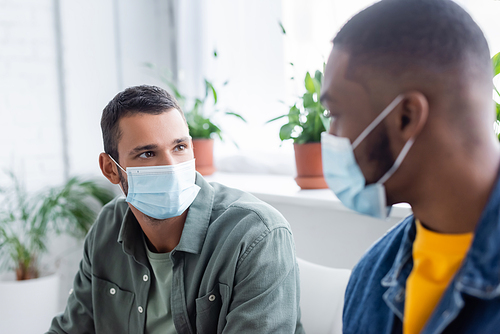 multiethnic men in medical masks talking in hospital, vaccination concept