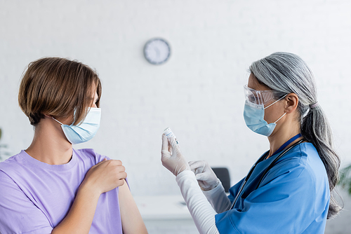 young man in medical mask near mature asian nurse holding jar with vaccine