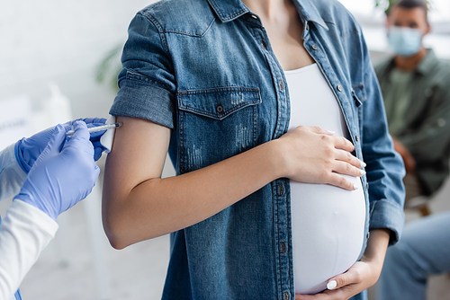 cropped view of doctor in latex gloves giving vaccine injection to pregnant woman in hospital