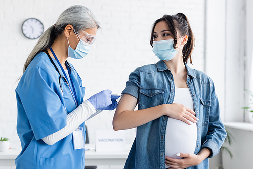 middle aged asian woman in medical mask and latex gloves vaccinating pregnant woman