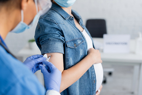 cropped view of blurred nurse vaccinating pregnant woman in clinic