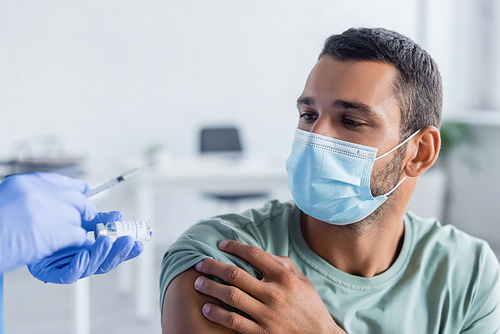 doctor holding syringe and jar with vaccine near young man in medical mask