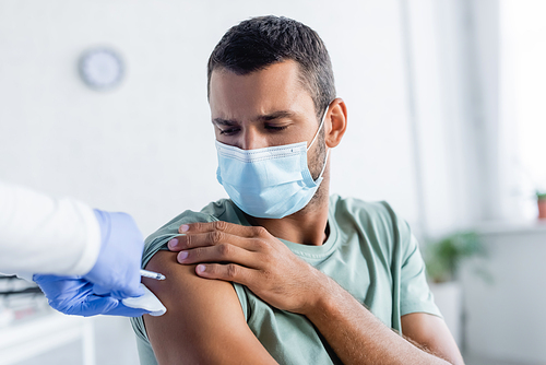 nurse in latex gloves vaccinating young man in medical mask