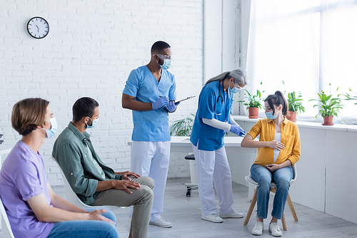 mature doctor vaccinating pregnant woman near african american colleague and patients