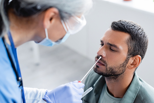 blurred nurse in medical mask taking samples for coronavirus test from young man