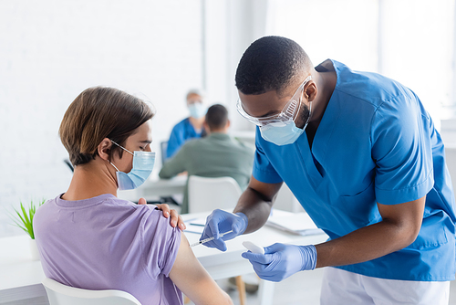 african american physician in medical mask and goggles vaccinating man in clinic