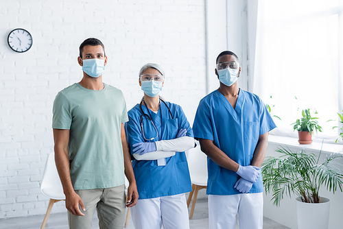 young man and interracial doctors in medical masks  in clinic, vaccination concept