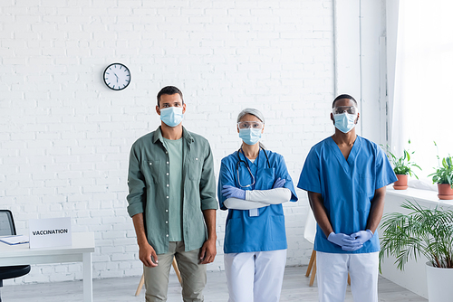 multiethnic doctors and young man in medical masks  in vaccination center