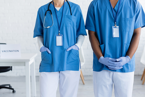 cropped view of interracial doctors in uniform with name tags in vaccination center