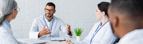 young doctor gesturing while talking to multicultural colleagues, banner