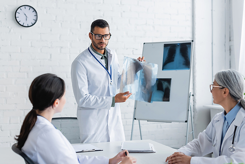 doctor in eyeglasses showing lungs x-ray to multiethnic colleagues during medical council