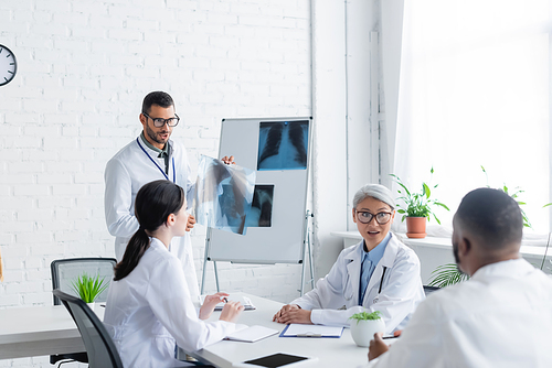 young doctor showing lungs x-ray to multiethnic colleagues during council