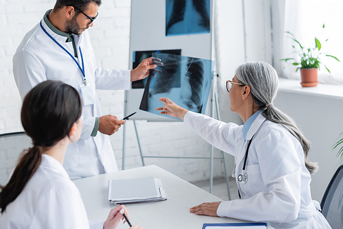 mature asian doctor pointing at lungs x-ray during meeting with young colleagues