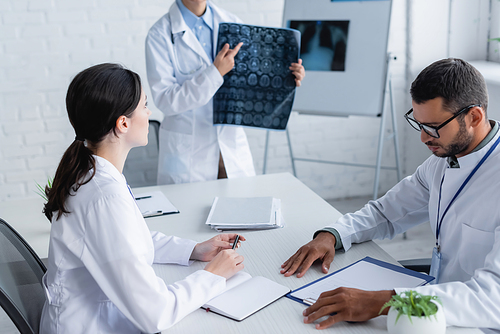 doctor pointing at brain mri scan near colleagues working with documents