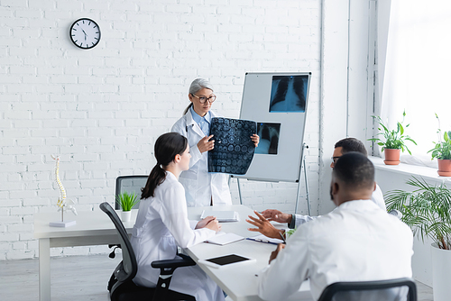 middle aged asian doctor holding head mri scan near multiethnic physicians in meeting room