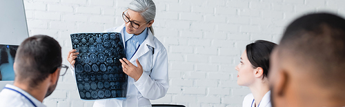 middle aged asian doctor showing brain mri scan to blurred multiethnic colleagues, banner