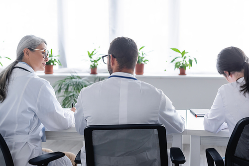 back view of young physicians sitting near mature asian doctor in meeting room