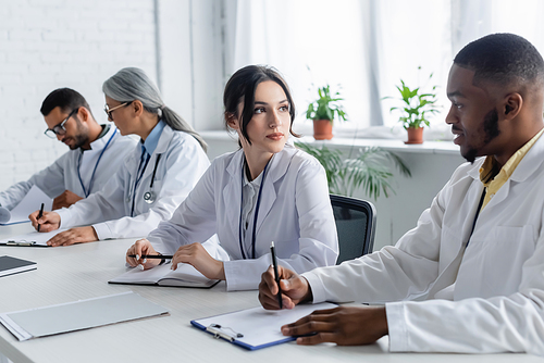 interracial doctors looking at each other near blurred colleagues