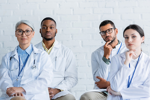 concentrated multiethnic doctors in white coats sitting during conference