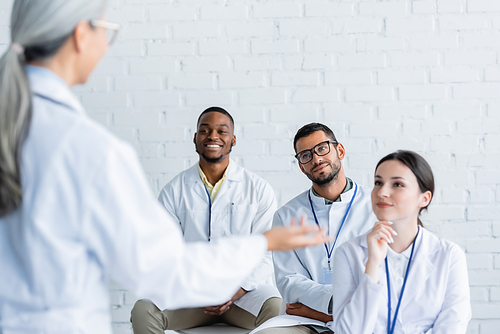 blurred middle aged doctor pointing with hand near young and positive physicians