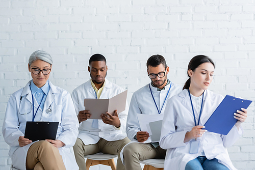 multiethnic doctors in white coats looking at documents during conference