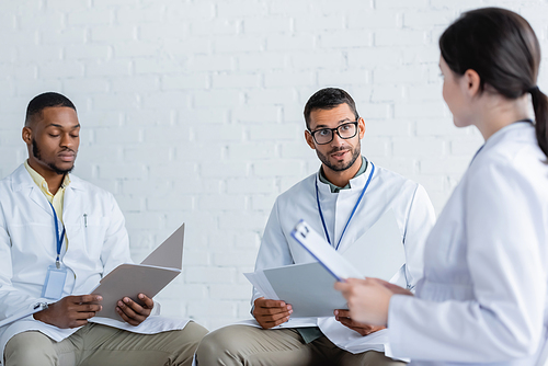 surprised physician in eyeglasses talking to multiethnic colleagues during conference