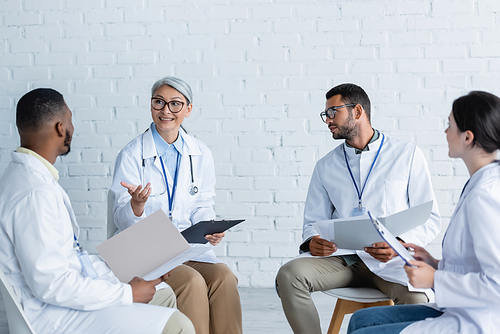 smiling asian doctor pointing at african american colleagues during medical council