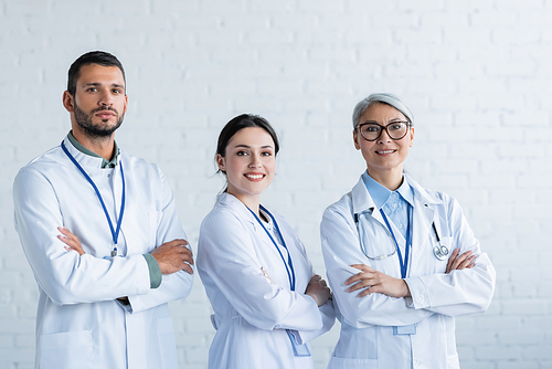 happy multiethnic doctors in white coats  while standing with crossed arms