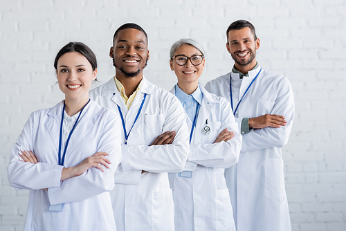 cheerful multiethnic physicians standing with crossed arms and smiling at camera