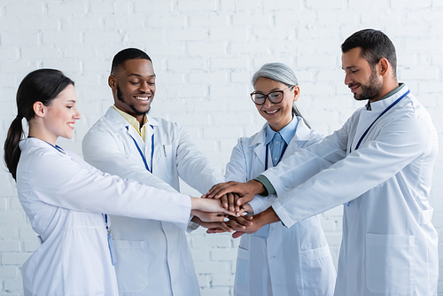 joyful multiethnic doctors standing with joined hands in clinic