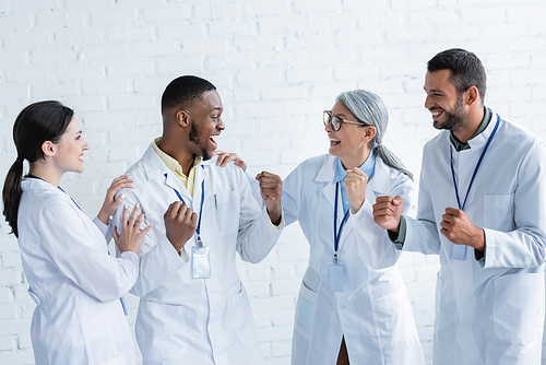 overjoyed multicultural doctors smiling at each other while showing win gesture