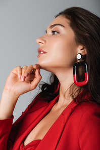 side view of trendy woman in red suit and earring posing isolated on grey