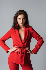 stylish woman in red suit posing and  while posing with hands on hips isolated on grey