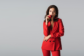 trendy young woman in red suit posing with fresh apple isolated on grey