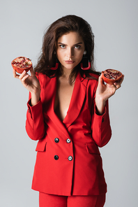 stylish woman in trendy suit holding red pomegranate halves isolated on grey