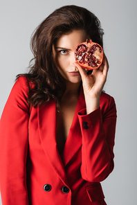 young woman in suit holding red pomegranate half isolated on grey