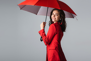 happy young woman in red suit standing under umbrella isolated on grey