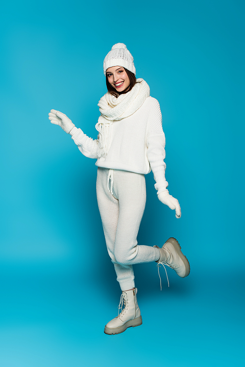Smiling woman in white sweater, scarf and hat  on blue background