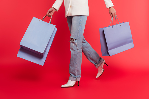 Cropped view of stylish woman holding shopping bags on red background
