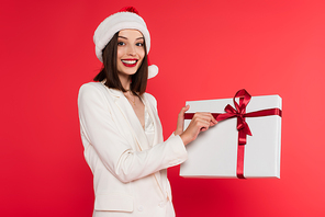 Smiling woman in santa hat holding gift with bow isolated on red