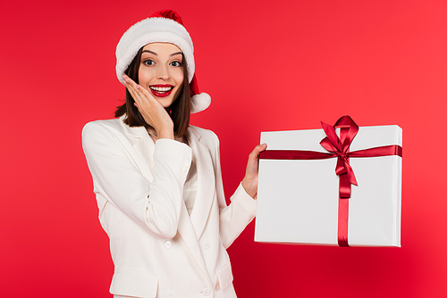 Excited woman in santa hat holding present isolated on red